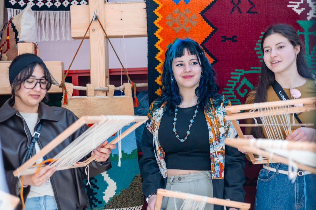 Participants holding their frame looms among traditional textiles