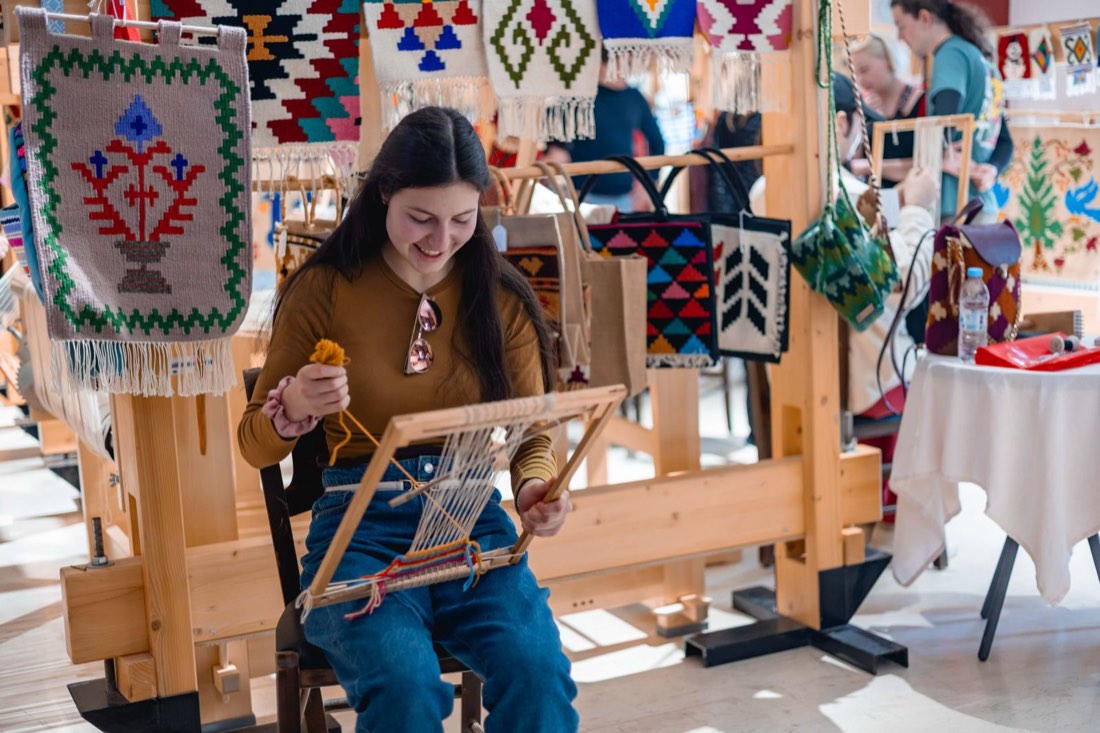 A participant smiling while weaving on a frame loom