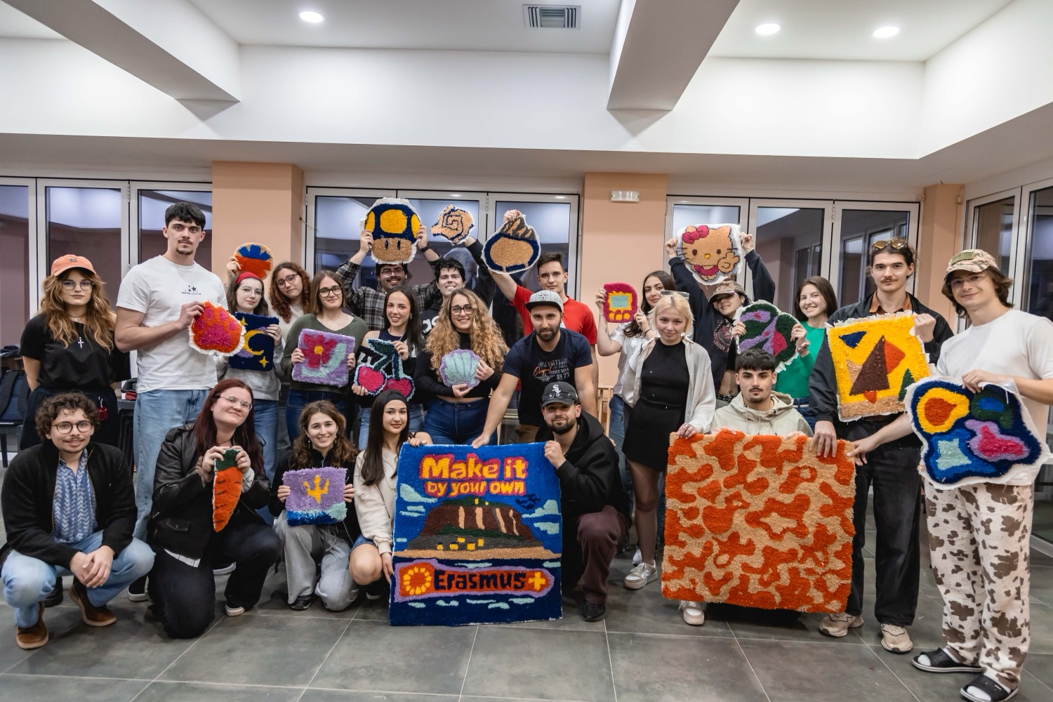 The whole group of 34 participants and team leaders holding the tufted rugs they made by hand, including the 'Make it by your own' Erasmus+ piece